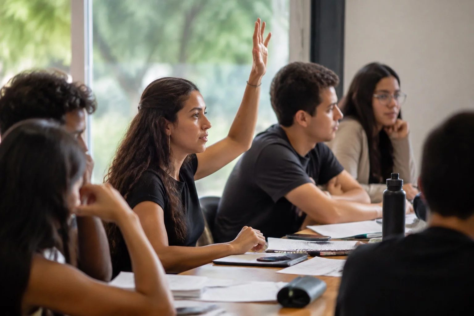 Estudante levantando a mão em uma mesa de seminário coberta de anotações