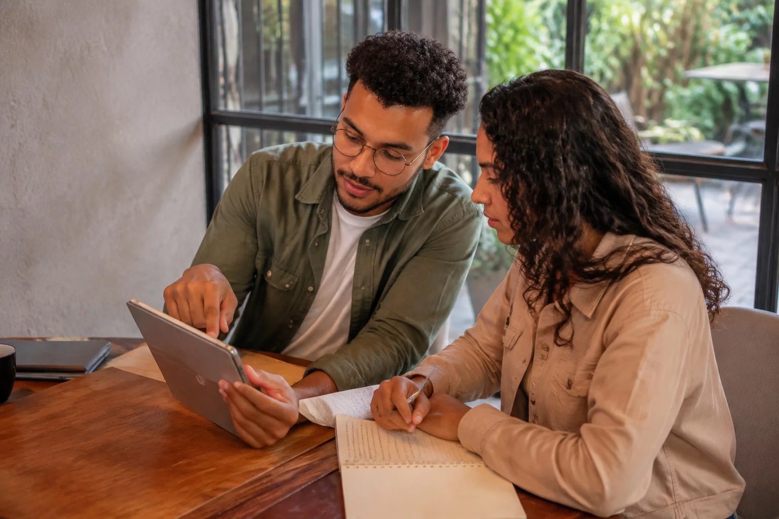Duas pessoas revisando anotações em um tablet sobre uma mesa de madeira